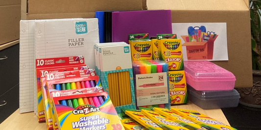 Table filled with school supplies including colored markers, pencils, paper and pencil boxes